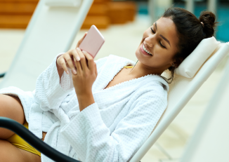 woman lounges in chair at a pool looking at phone